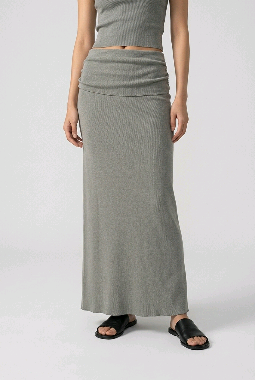 Person wearing a dark gray long skirt and crop top on a white background