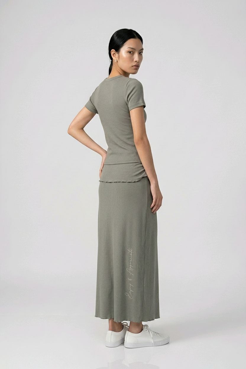 Woman wearing a dark grey skirt and top with a plain background